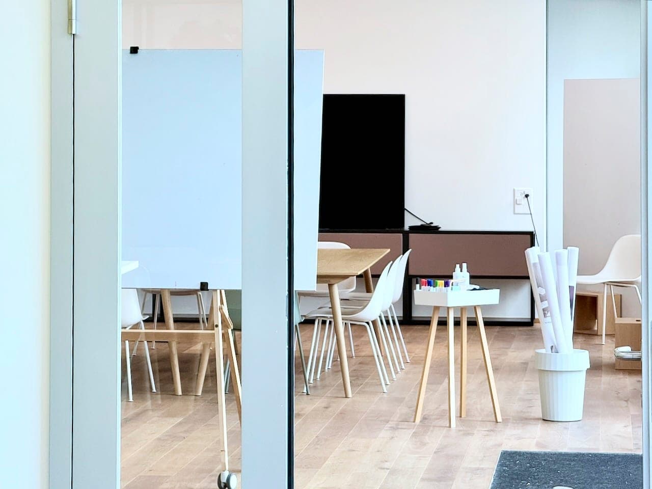 Blick durch die Glastüre in die Pure Arena in Luzern: Workshoptisch, Whiteboard, Screen und Moderationsmaterial