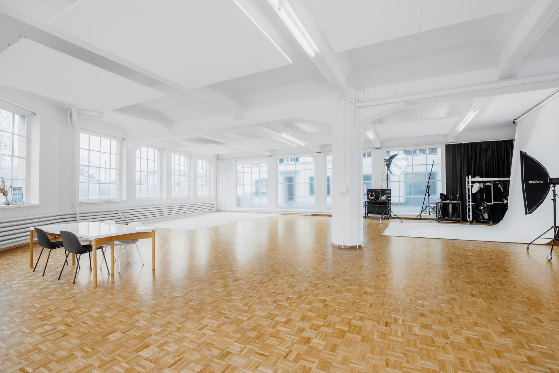 The Studio in Luzern: heller Saal mit Parkett, hohen Sprossenfenstern und Fotohohlkehle mit Studiolicht