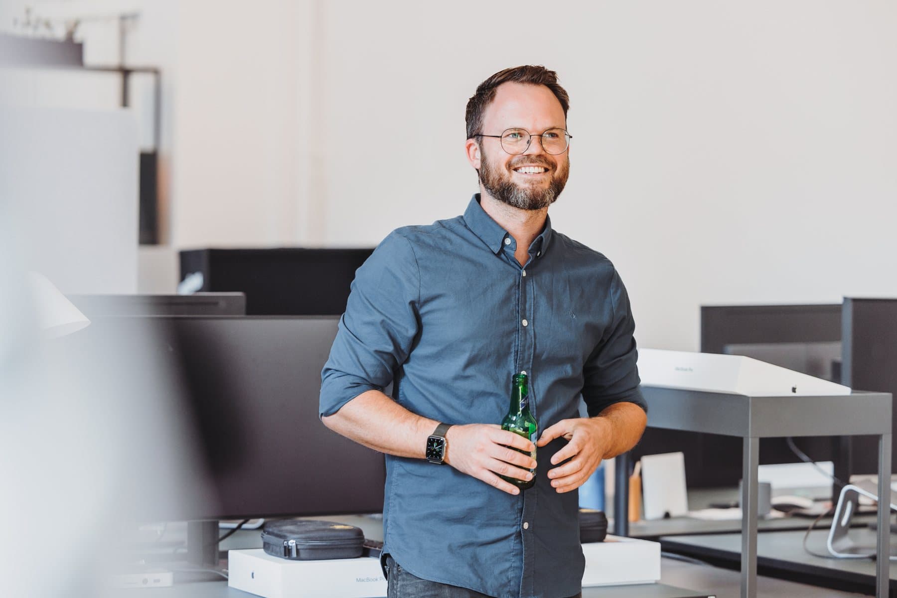 Lachende Person mit einer Flasche in der Hand zwischen Arbeitsplätzen